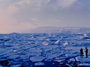 man and woman standing cracked sea ice under gray sky