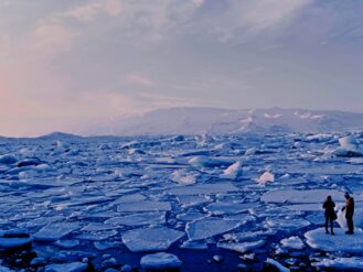 man and woman standing cracked sea ice under gray sky